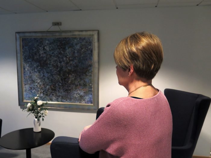 Marianne katsoo eteenpäin, niin että me näemme hänestä vain sivuprofiilin. Pöydällä on kukkia, seinällä tummasävyinen taulu.
